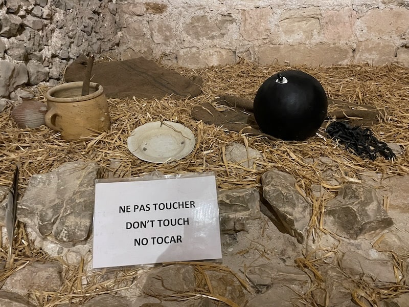 Historical recreation of Edmond Dantes' cell at Chateau d'If, Marseille, with "Do not touch" reminder for visitors.