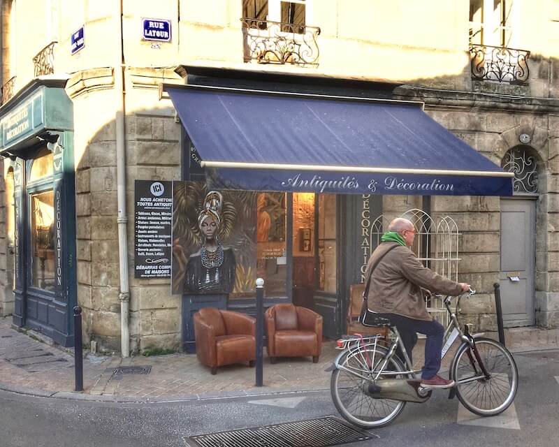 Man on a bicycle passing an antique shop in Bordeaux France